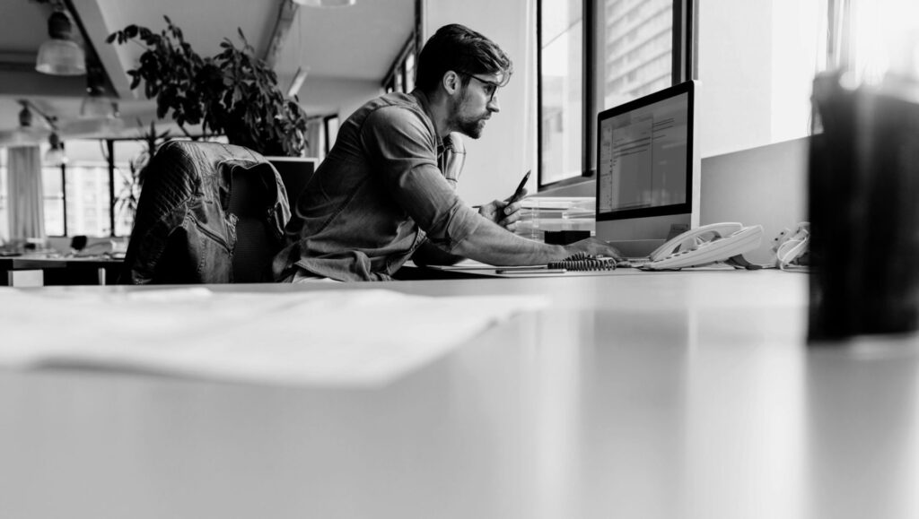 Young man sitting in office and working on desktop pc. Businessman looking at computer monitor while working in office.