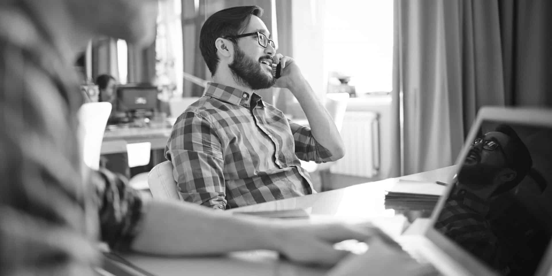 Young businessman sitting by workplace and speaking on the phone